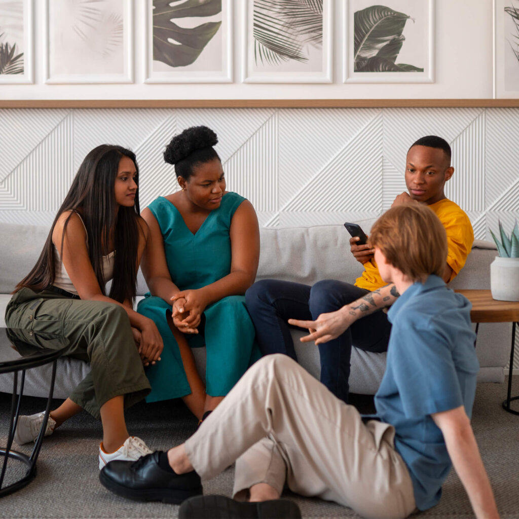 Three friends sat on the sofa, while one friend is sat on the floor, enjoying each other company talking.