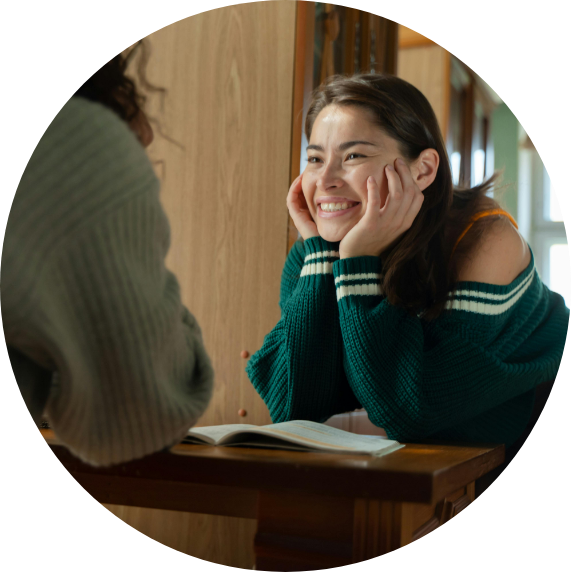 A young woman resting her face in her hands smiling at another person
