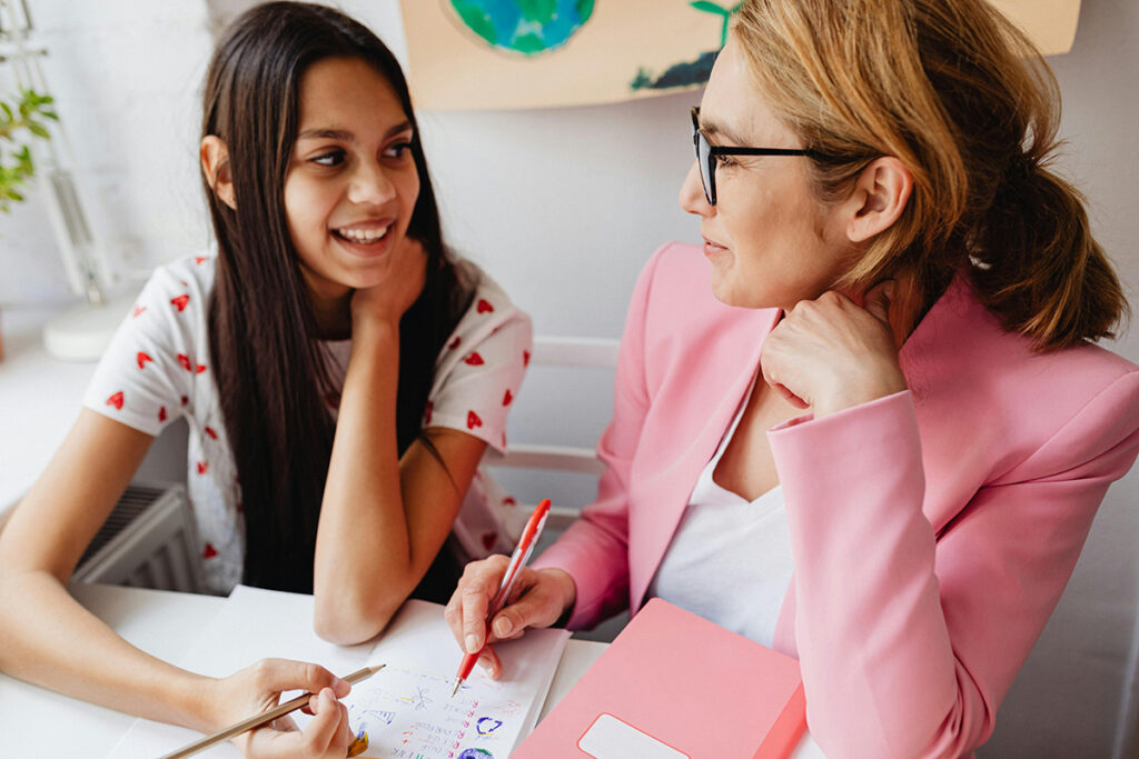 A teacher and student looking at each other and smiling as the teacher is helping the student