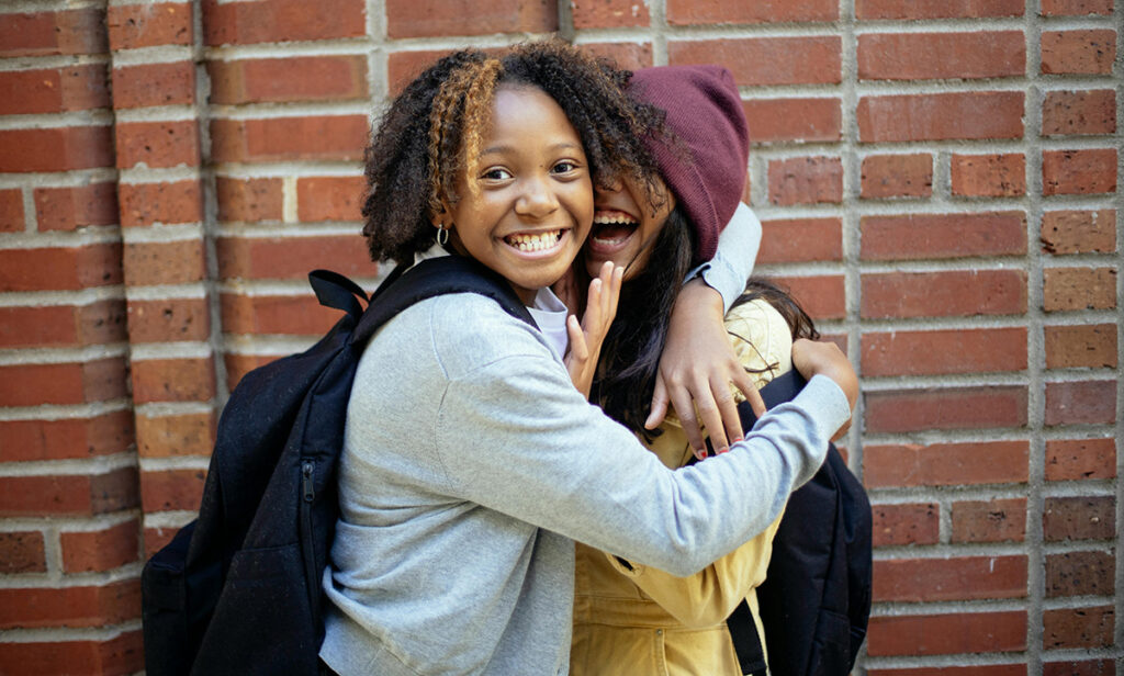 Two teenagers smiling and laughing while hugging eachother