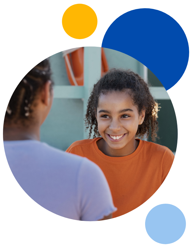 Young child, wearing a orange t-shirt, smiling at another child in a circle with blue, yellow and light blur circles surrounding them.