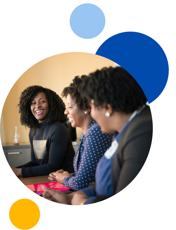Three woman sat work table, laughing and talking in a circle with blue, yellow and light blur circles surrounding them.