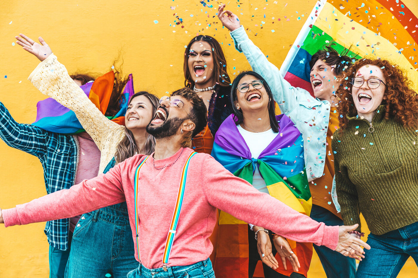 A group of young people celebrating together with a Pride flag and confetti